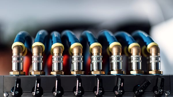 A row of blue hoses with brass and chrome quick-connect couplings above a rail of black lever valves