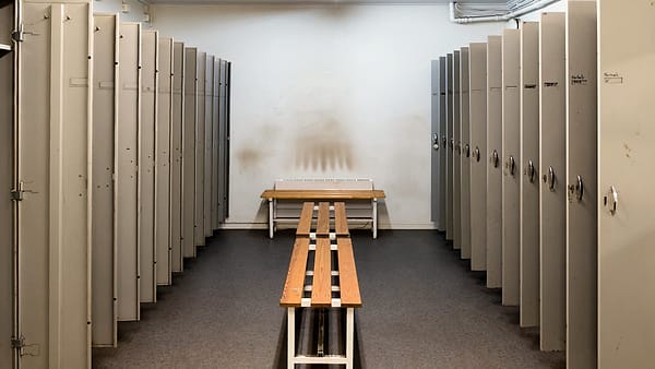Two rows of tall gray metal lockers facing each other across a narrow changing room with wooden benches