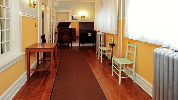 An empty hallway with a wooden table along one wall and two pale green ladder-back chairs facing it