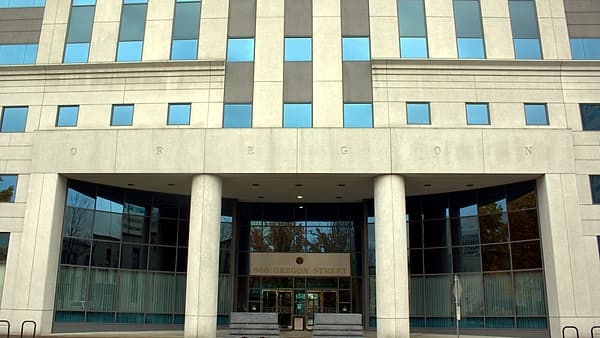 A pale stone office building with tall columns framing a glass entrance, the word OREGON carved across the facade