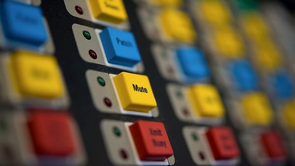 Close view of a control panel of red, yellow and blue square buttons, one labeled Mute in sharp focus