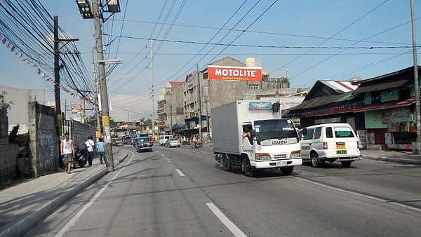 A row of small roadside shops and stacked goods along a wide highway shoulder.