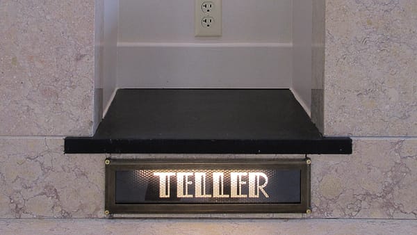 A glowing brass-framed sign reading TELLER set into a marble counter recess below a black stone ledge