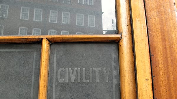 A weathered wooden window frame holding a frosted glass pane etched with the single word CIVILITY