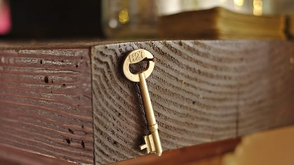 A small brass skeleton key hanging on a nail against the grain of a dark wooden mantel beam