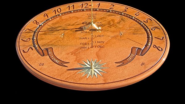 A round stone sundial face carved with hour numerals, a month scale and an inlaid gold compass star