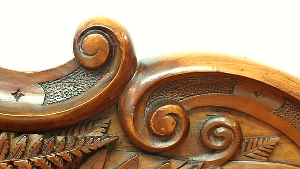Carved wooden scrollwork with two facing spiral volutes above fern leaf motifs against a plain white background