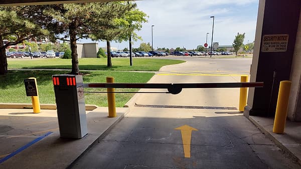 A lowered barrier arm blocking a garage entrance lane, with yellow bollards and a painted arrow on the asphalt