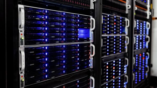 An angled view down a data center aisle of rack-mounted servers glowing with blue and occasional red status lights
