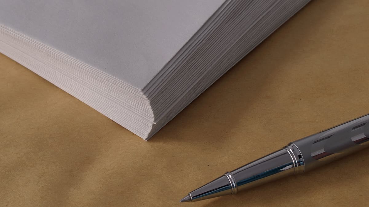 A silver rollerball pen resting on tan paper beside the corner of a thick stack of white sheets