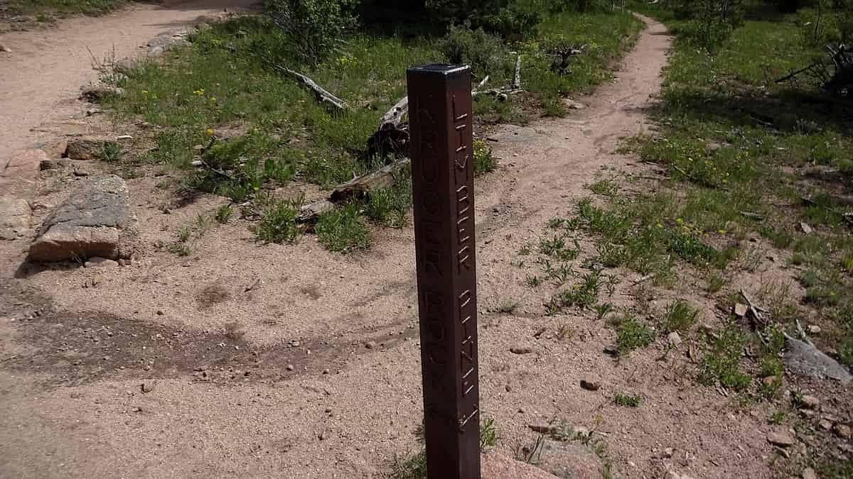 A weathered wooden marker post with carved lettering standing where a dirt trail forks into two paths