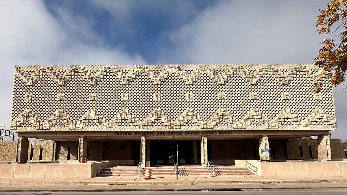 A long low building fronted by a patterned pierced stone screen above concrete columns and entrance steps